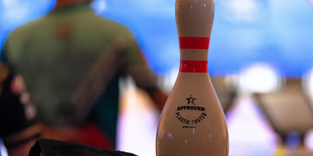 Bowling pin standing on a table in a bowling alley in front of a bowing player who is getting ready for a shot